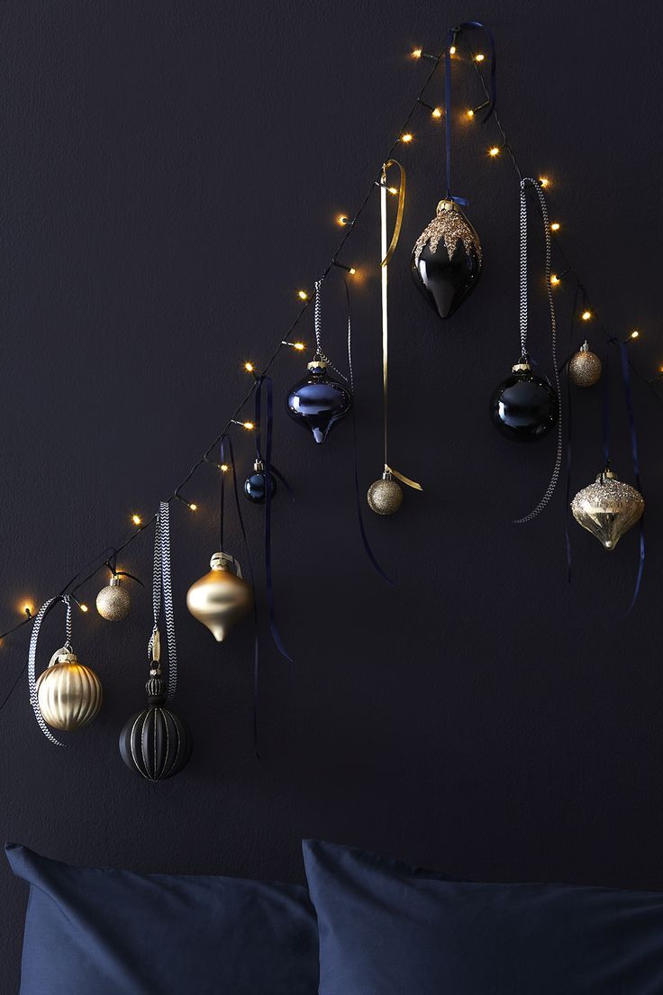 christmas ornaments hanging on the wall above a bed with blue sheets and pillows, along with string lights