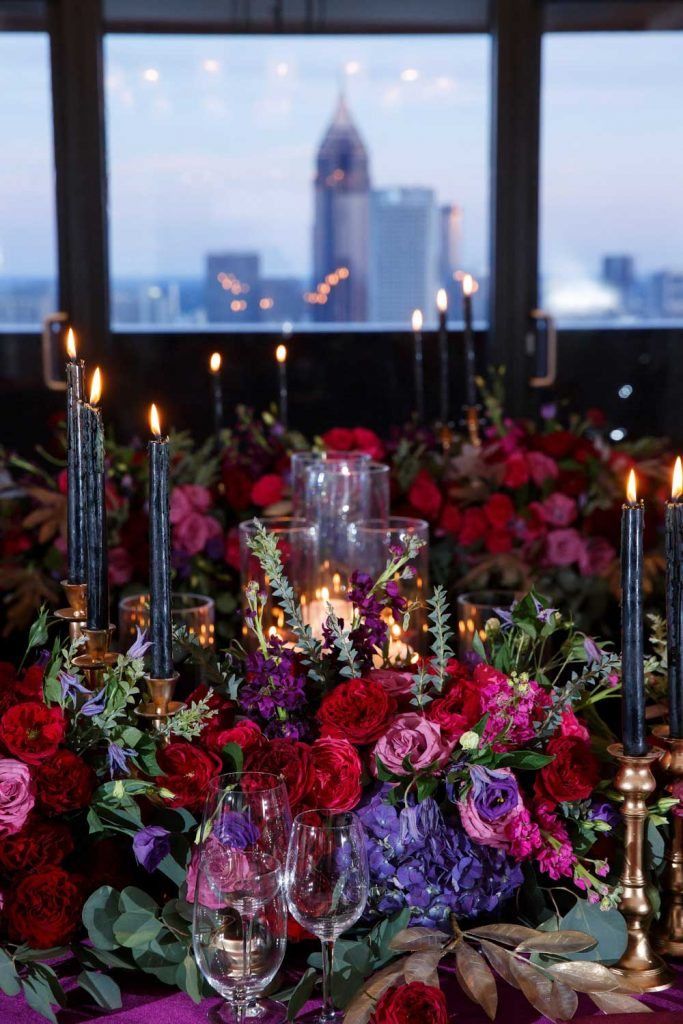 the table is set with candles, flowers and wine glasses in front of large windows