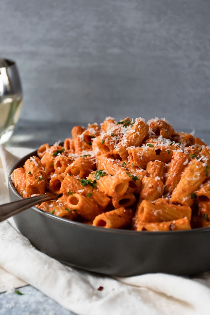 a bowl full of pasta with parmesan cheese on top and a glass of wine in the background