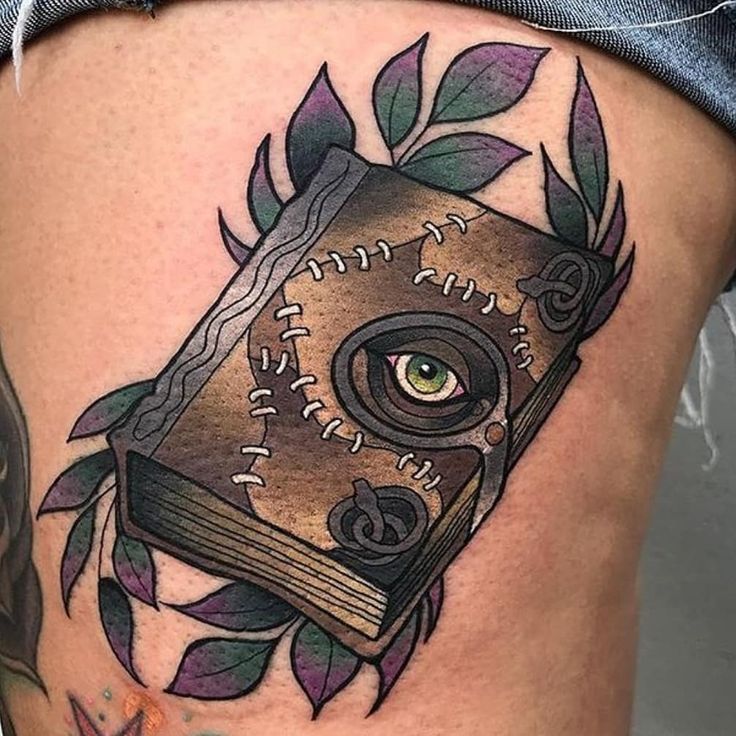 a woman's thigh with a book tattoo on it and an eye in the middle