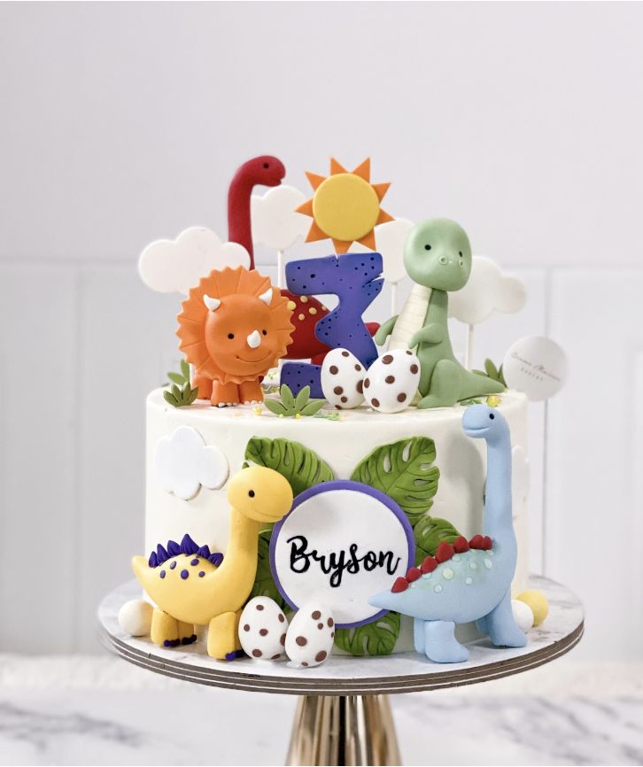 a birthday cake decorated with dinosaurs and name on the top is sitting on a stand