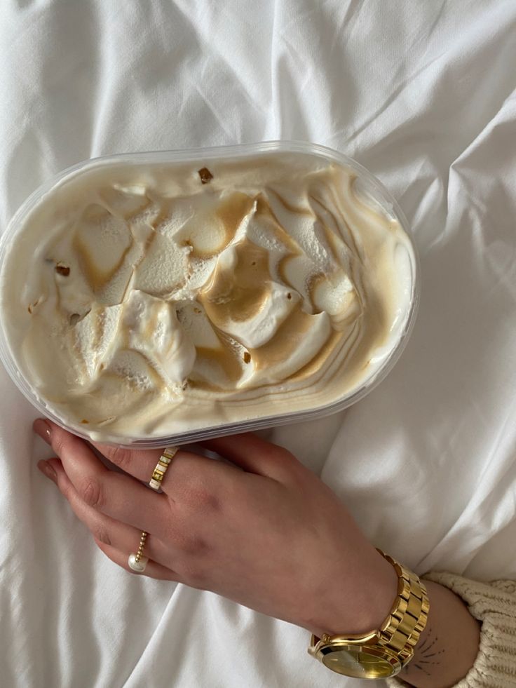 a woman's hand holding a container of food on top of a white sheet