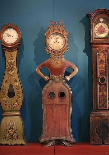 an assortment of antique clocks on display in a museum case with blue walls behind them