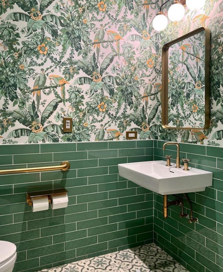 a green tiled bathroom with gold fixtures and mirror above the sink, along with two toilet paper rolls