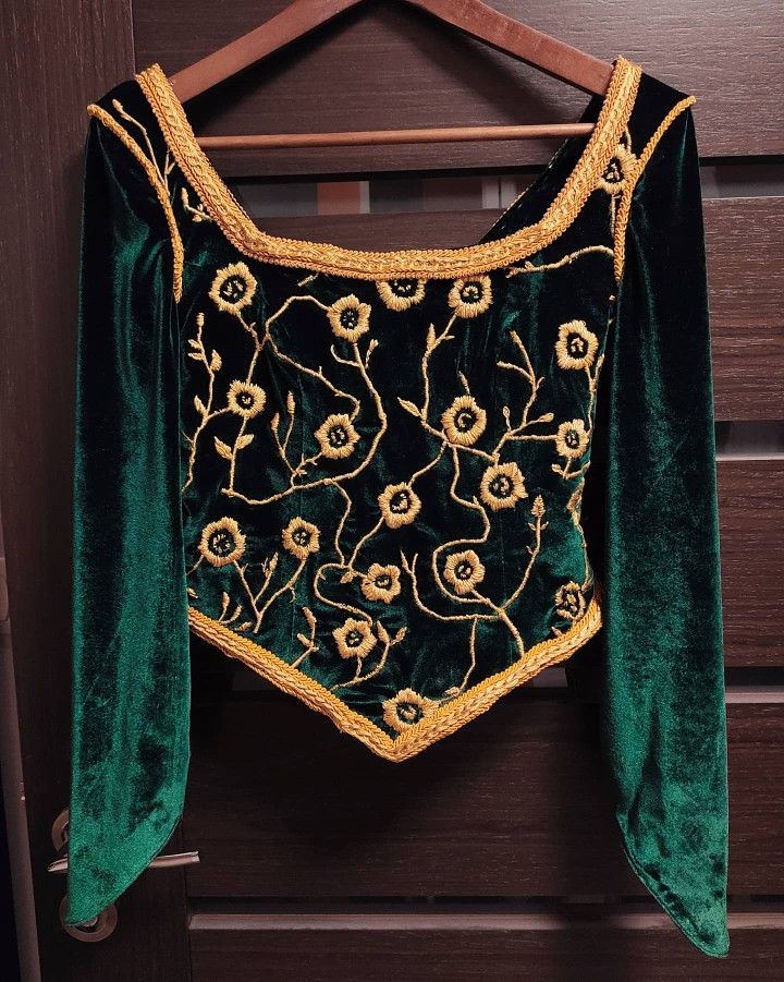 a green velvet top with gold embroidered flowers on it hanging from a wooden hanger