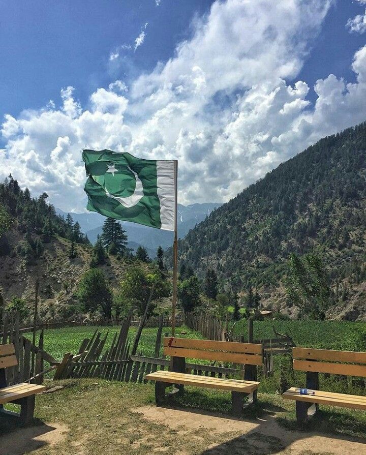 a flag flying in the wind on top of a field next to benches and mountains