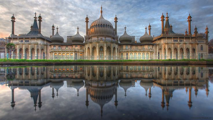 a large building sitting next to a lake under a blue sky with clouds in the background