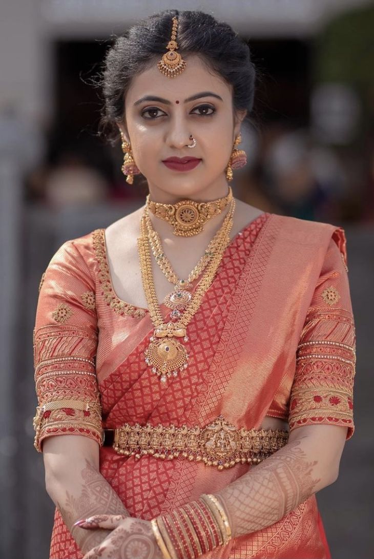 a woman in an orange and gold sari with jewelry on her neck, standing outside