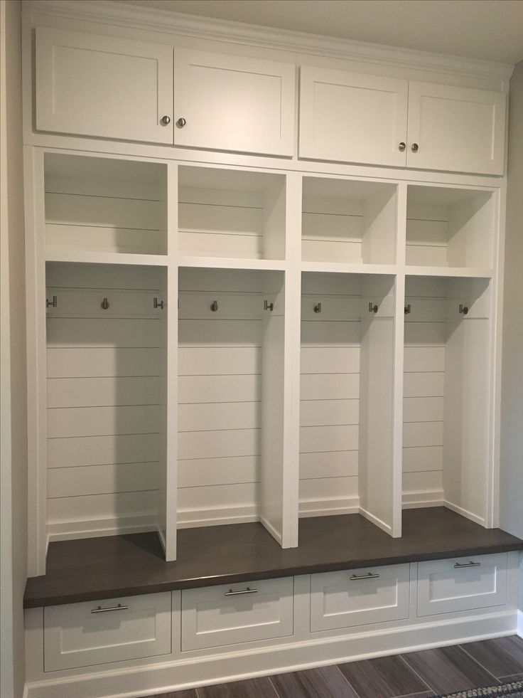 an empty white mud room with built - in cabinets and drawers on the wall, along with wood flooring