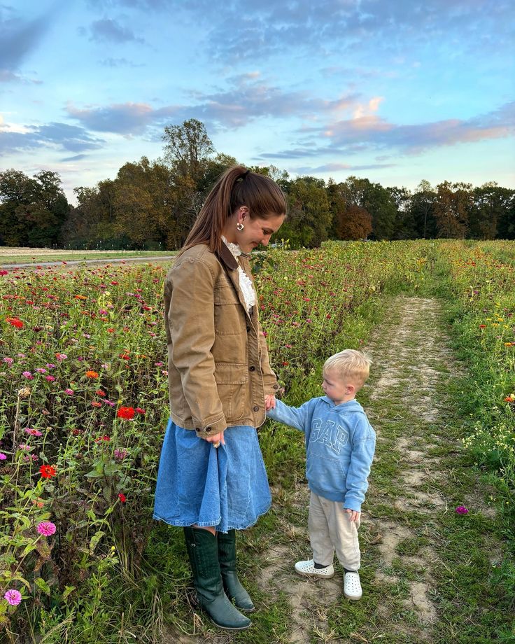 a woman holding the hand of a little boy in a field