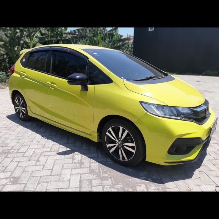 a bright yellow honda civic hatchback is parked in front of a black car on a brick driveway