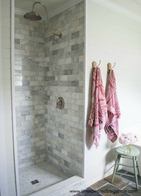 a bathroom with a walk in shower next to a white stool and towel on the wall