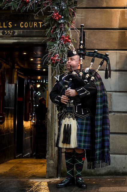 a man in a kilt playing the bagpipes outside a building with a wreath on it