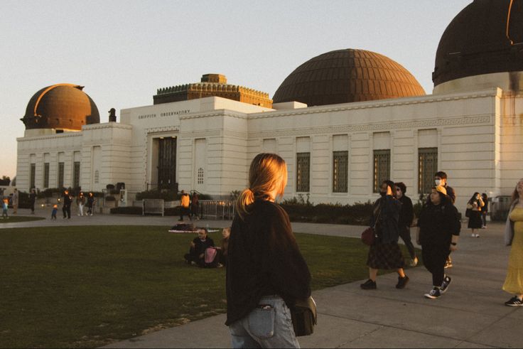 people walking around in front of a building with domes on the roof and grass area