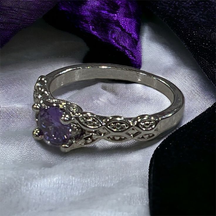 a close up of a ring on a white cloth with a purple ribbon in the background