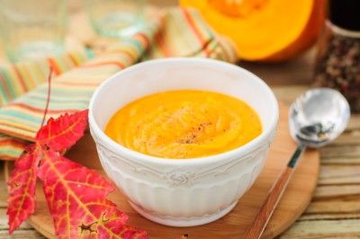 a white bowl filled with carrot soup next to a spoon and orange leaves on a cutting board