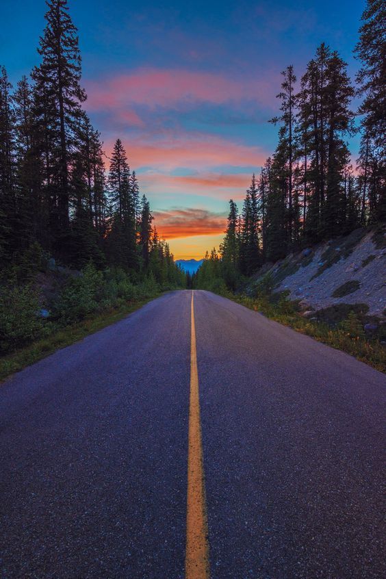 an empty road with trees and mountains in the background at sunset or sunrise hours ago