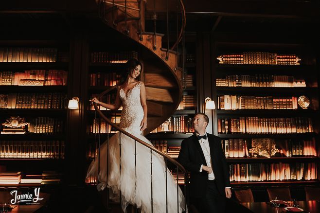 a bride and groom standing on the stairs in front of bookshelves at night