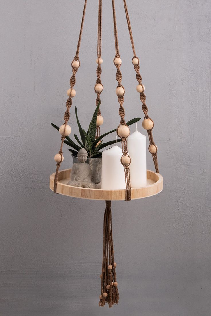 a wooden tray with candles and some plants on it, hanging from the ceiling in front of a gray wall