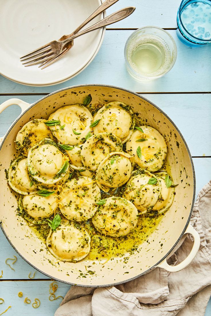 a skillet filled with dumplings on top of a wooden table next to plates and utensils