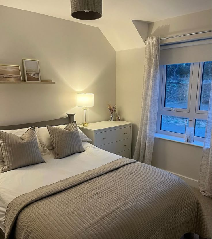 a bed sitting under a window next to a night stand with two lamps on top of it