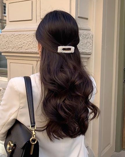 a woman with long dark hair wearing a white shirt and carrying a black purse