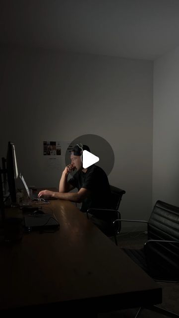 a man sitting in front of a computer on top of a wooden desk next to a black chair