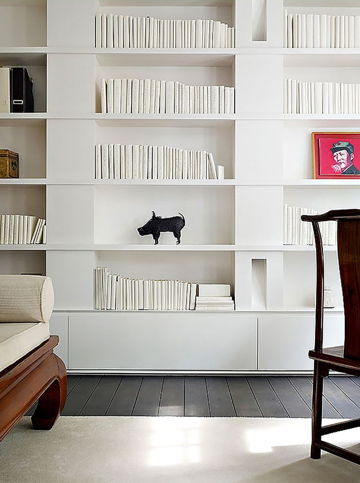 a living room with white bookshelves filled with books and a black dog figurine