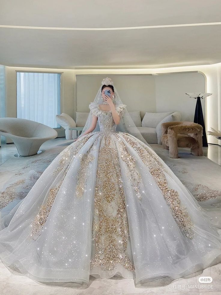 a woman in a white and gold wedding dress standing in a room with large windows