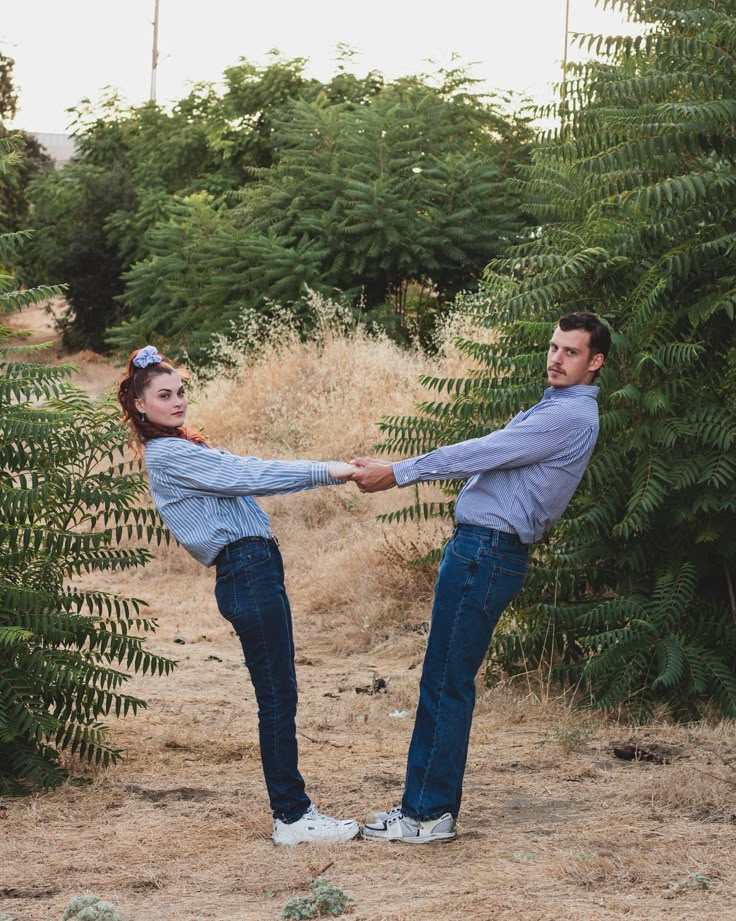 a man and woman holding hands while standing in the middle of a tree lined field