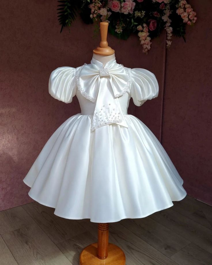 This pretty handmade dress is perfect for flower girls, junior bridesmaids, christenings, or any special occasion--even for dress-up fun! Bodice: Adorned with a full bow and pearl embellishments, featuring a polyester lining and a high-quality hidden back zipper for a polished look. Skirt: Light champagne satin with a soft polyester lining, complemented by the bodice bow that ties beautifully at the waist. Lining: Soft cotton lining ensures all-day comfort. Designed to knee length as standard, b Satin A-line Dress With Bow, Elegant Dresses With Bow Print, Spring Princess Dress With Bow For Dress-up, Elegant Short Sleeve Princess Dress For Dress-up, Spring Satin Dress For Dress-up Occasions, Short Sleeve Princess Dress With Bow For Party, Fitted Princess Dress With Bow For Dress-up, Party Dress With Bow Print And Short Sleeves, Elegant Bow Print Dresses For Spring