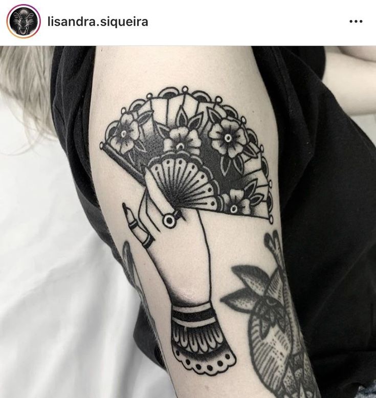 a woman's arm with a fan and flowers tattoo on her left arm, which is black and white