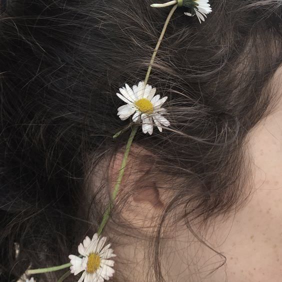 the back of a woman's head with three daisies in her long hair