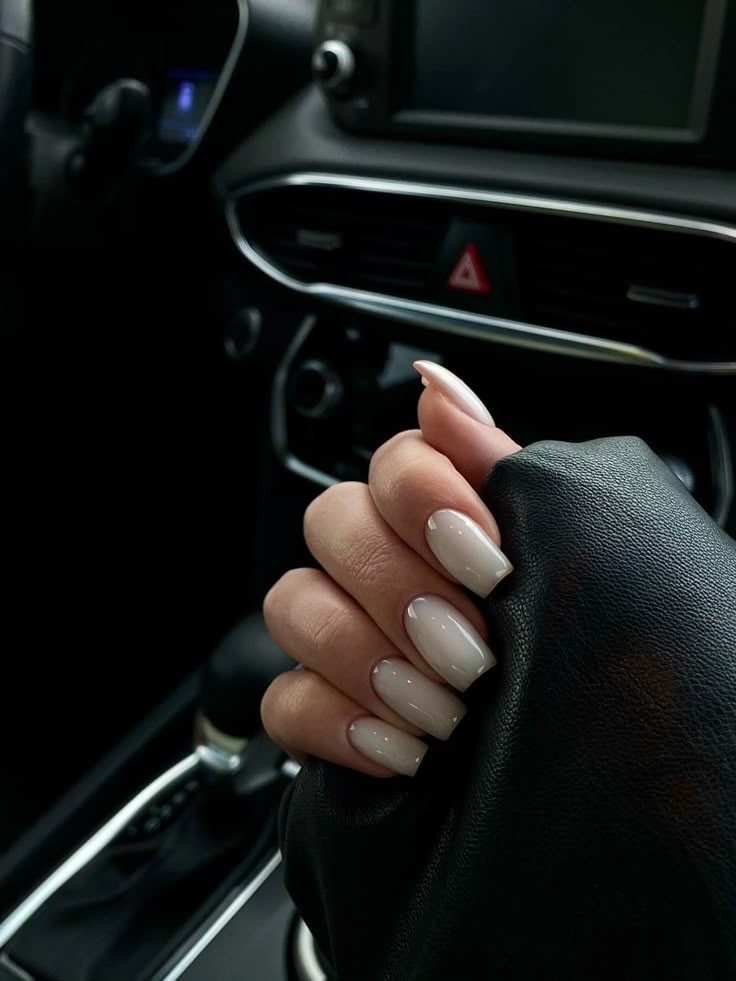 a woman's hand on the steering wheel of a car, with white nails