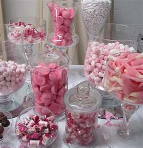 a table topped with lots of pink and white candies next to glass vases