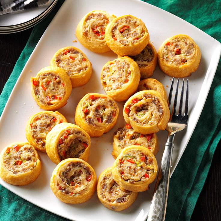 a white plate topped with mini pizzas on top of a green cloth next to a fork