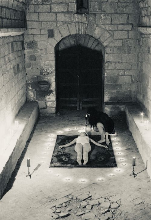 a woman kneeling down on a rug in an old building with candles lit up around her