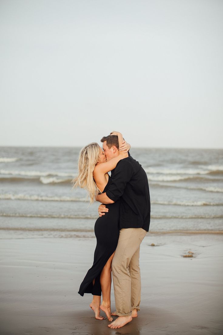 a man and woman kissing on the beach with waves in the backgroound