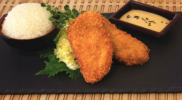 fried fish with rice and sauce on a black plate