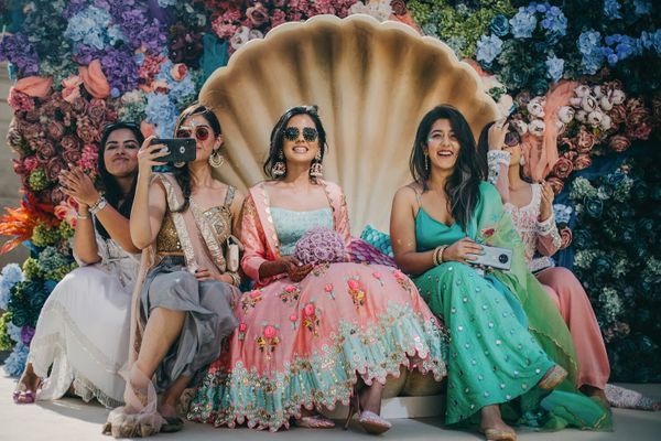 three women sitting on a shell with flowers in the background and one woman taking a selfie