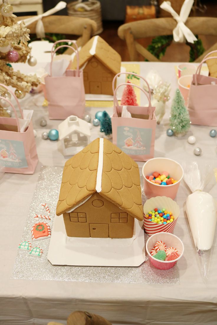 a gingerbread house shaped cake on a table with candy and other treats around it