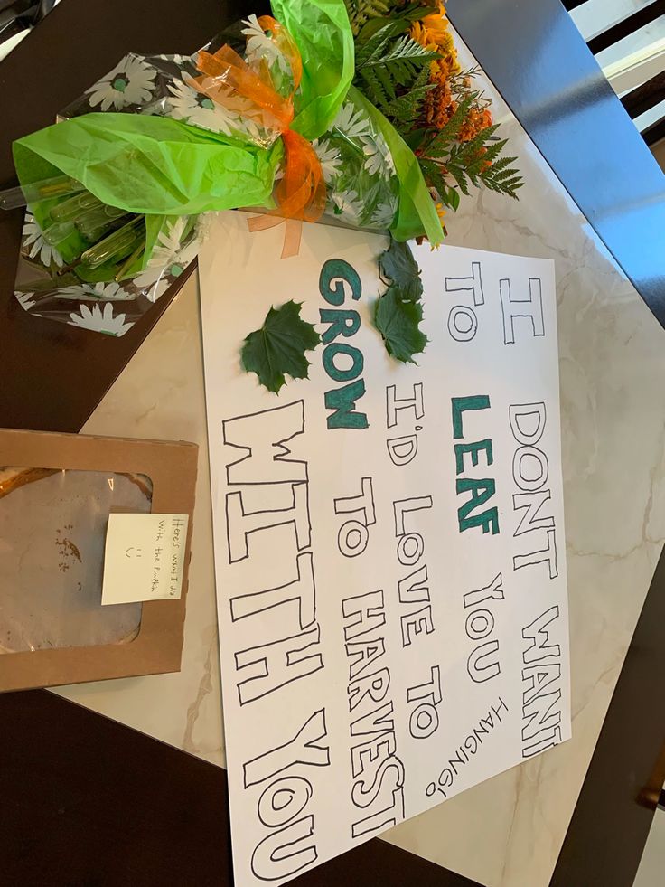 a sign sitting on top of a wooden table next to flowers and paper bag with writing