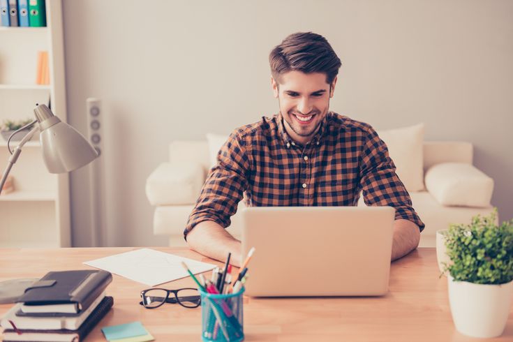 a man sitting at a table with a laptop computer in front of him and smiling