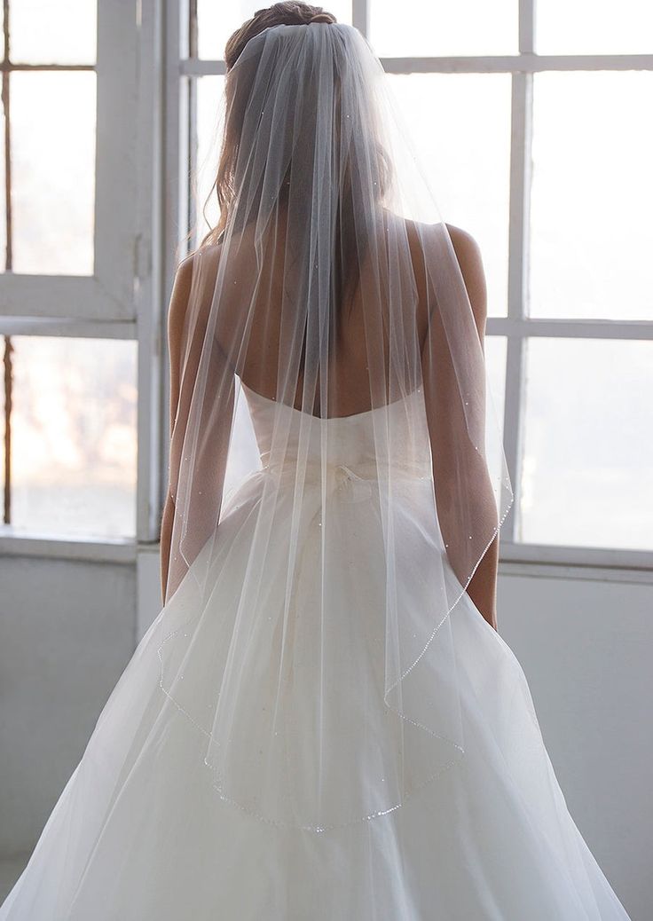 the back of a bride's wedding dress with a veil on her head and shoulders