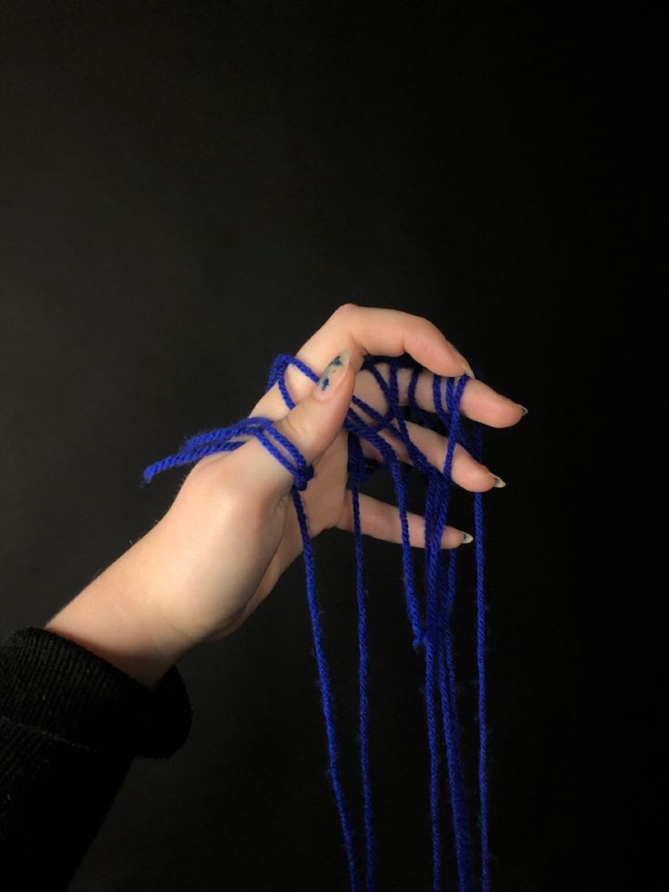 a woman's hand with blue string attached to her thumbnails, against a black background