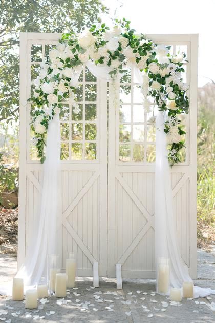 an outdoor wedding ceremony with white flowers and greenery on the door, candles in front of it