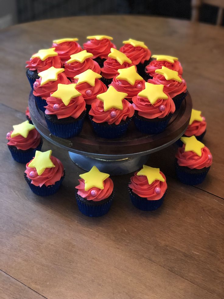 cupcakes with red, yellow and blue frosting are on a cake stand