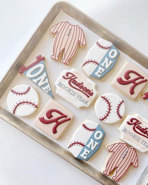 decorated cookies in the shape of baseballs and shirts on a baking sheet with words