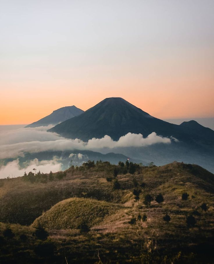 the sun is setting over some hills with clouds in the sky and trees on the ground