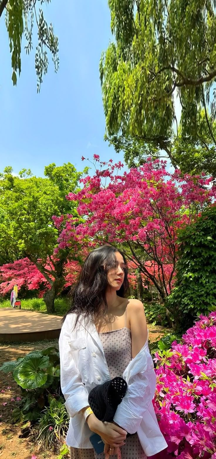 a woman holding a baby in her arms while standing next to pink flowers and trees